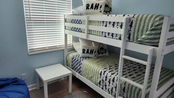 A bunk bed with patterned bedding, a small white table, and a blue bean bag chair in a room with light blue walls.