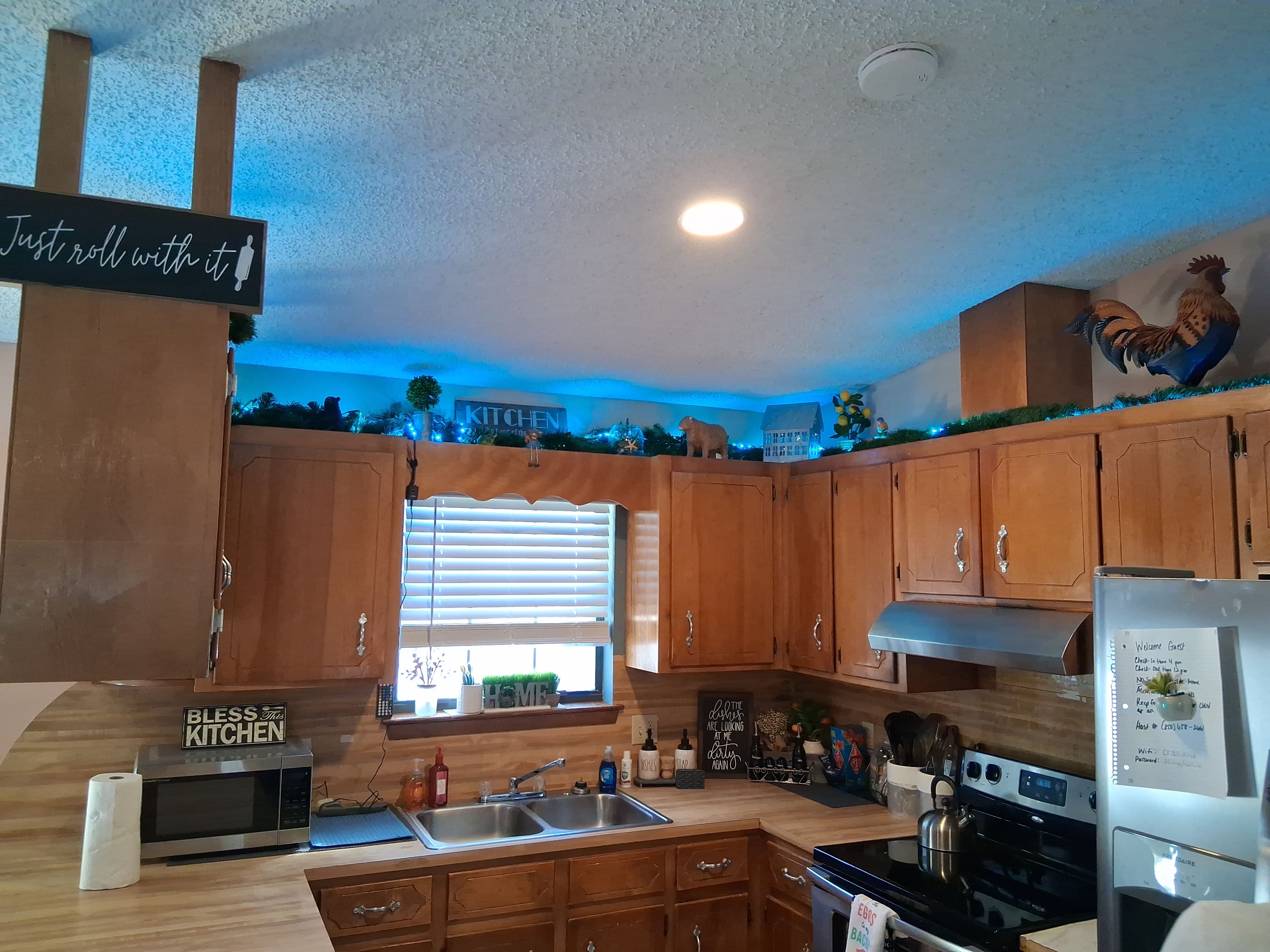 A kitchen with wooden cabinets, a stainless steel sink, a microwave, and a refrigerator.