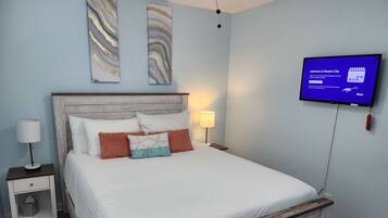 A bedroom with a bed, a nightstand, a TV, and wall art.