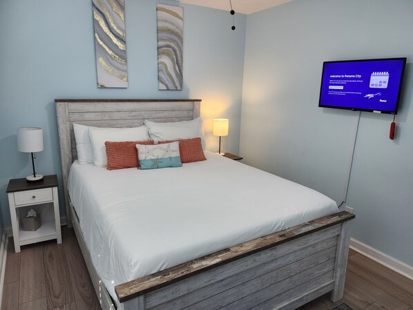 Um quarto com uma cama, mesa de cabeceira, televisão e obras de arte na parede.