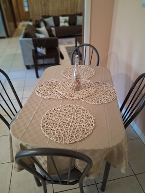 A dining table with a beige tablecloth, two circular placemats, and a clear glass bottle with a white cap.