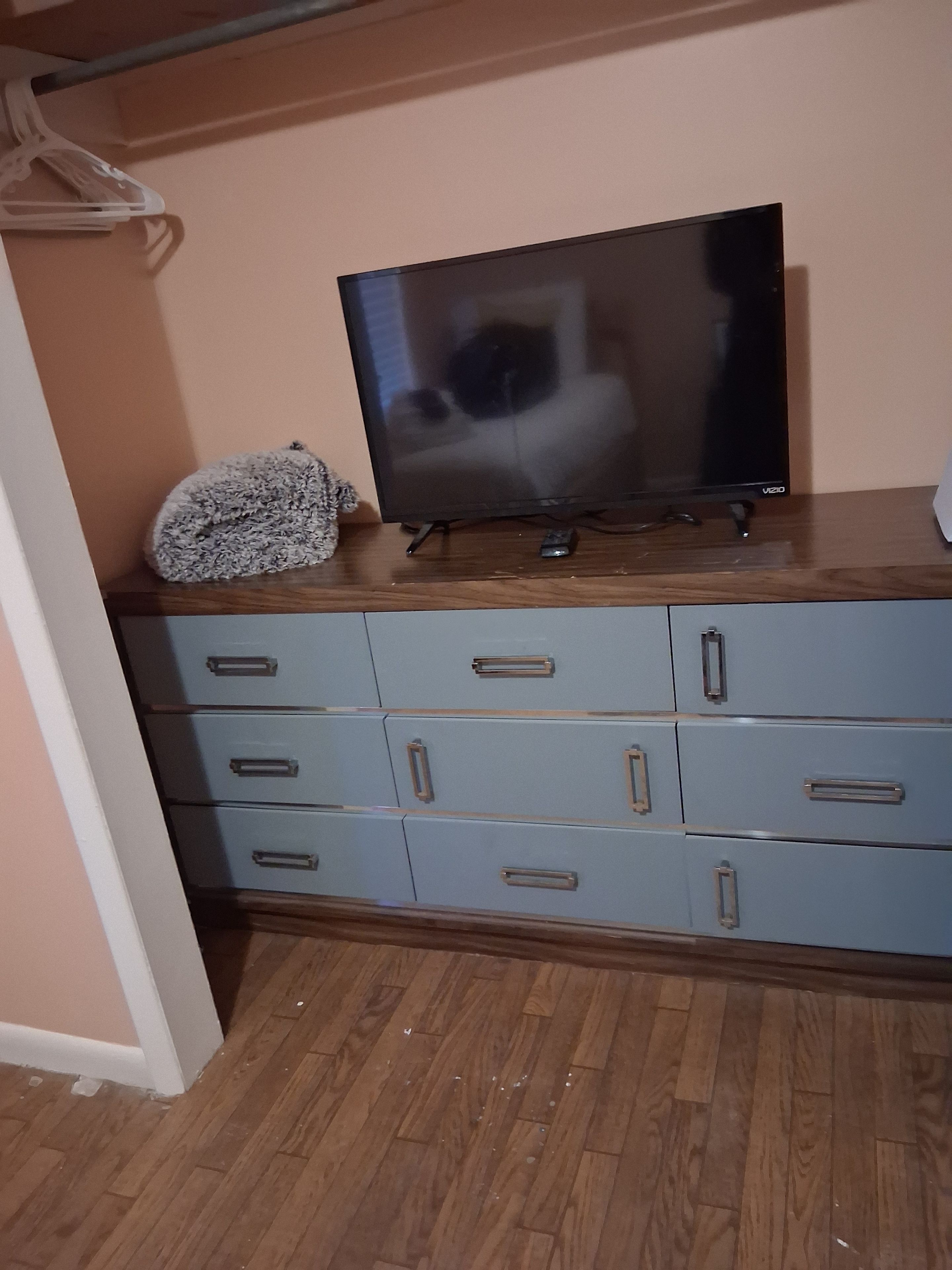 A room with a wooden cabinet, a television on top, and a fluffy object on the cabinet.