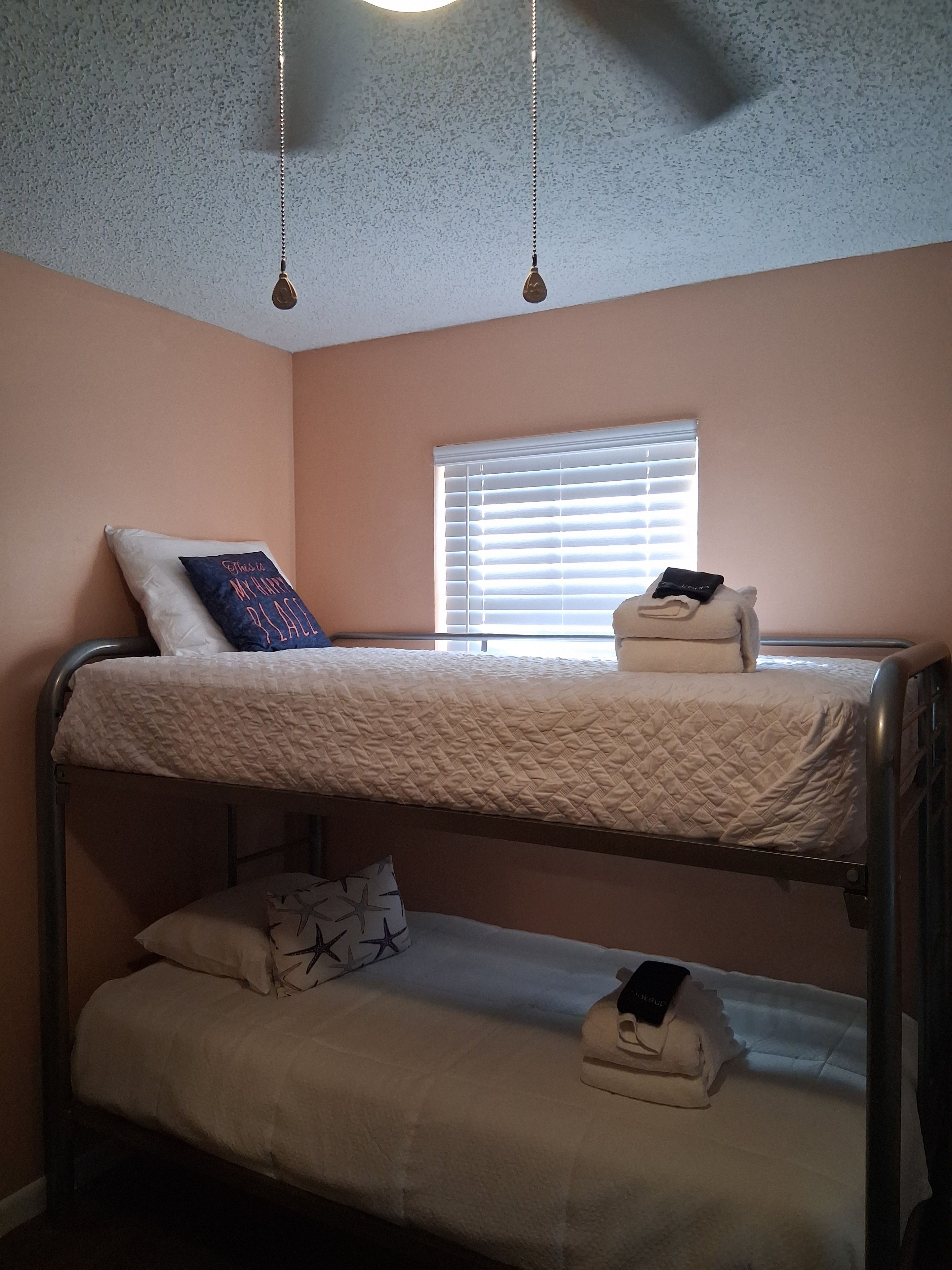 A bunk bed with a window above, a hanging light fixture, and a wall with a textured pattern.