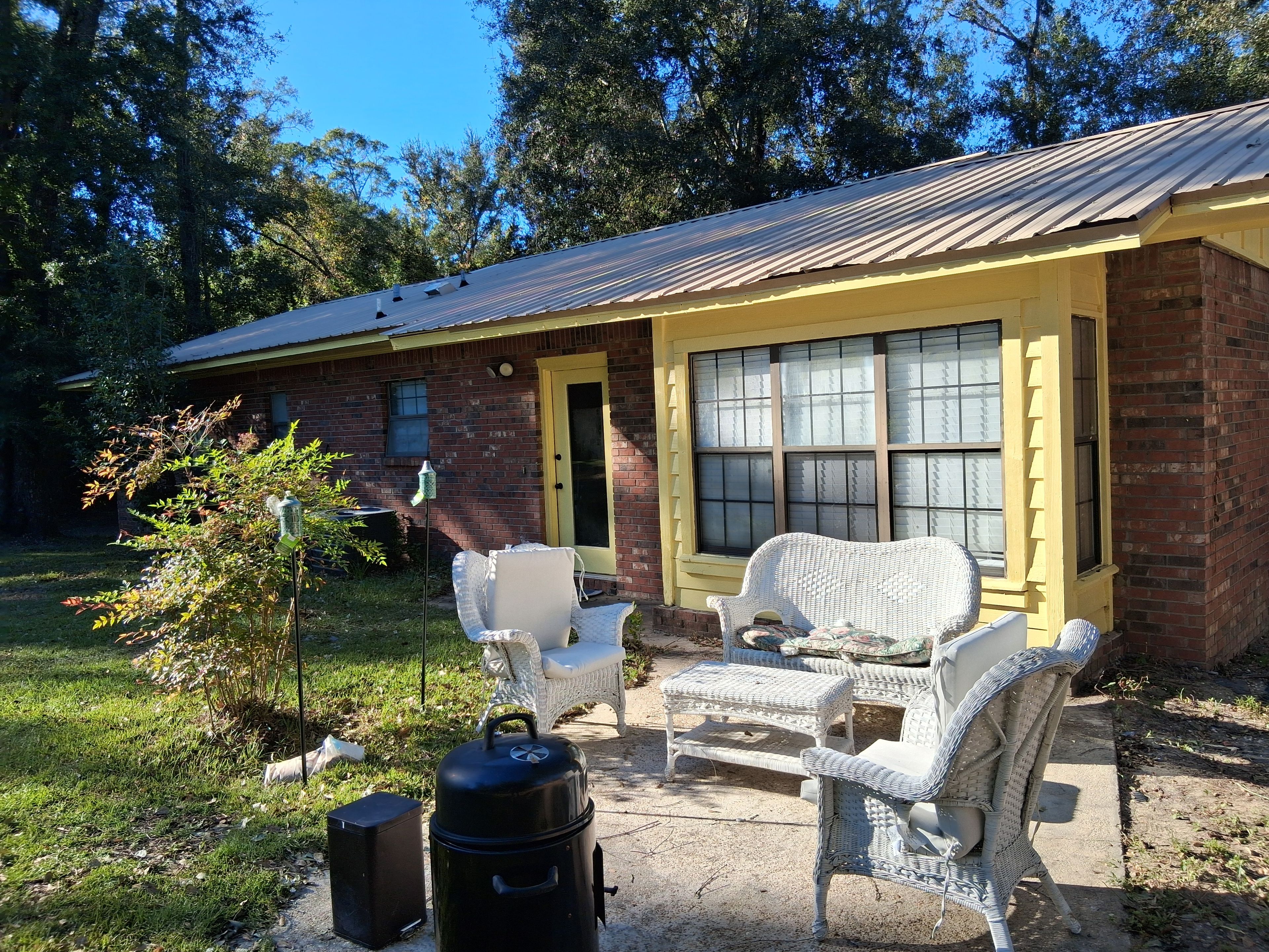 A brick house with a yellow front door and windows, outdoor wicker furniture, a grill, and a speaker.