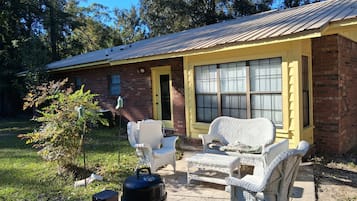 A brick house with a yellow front door and windows, outdoor wicker furniture, a grill, and a speaker.