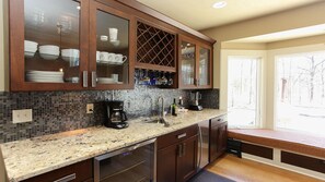 Una cocina con estante empotrado para vinos, cafetera y un asiento junto a la ventana.