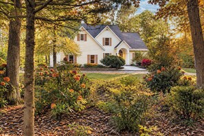 A two-story house with a symmetrical facade, a central entrance, and a well-maintained garden with various shrubs and flowering plants. - Riverwalk Retreat | Gather • Relax • Explore (Saugatuck)