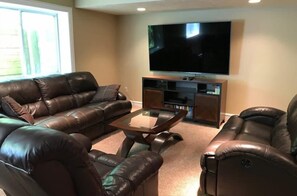 A living room with a leather sofa set, a coffee table, and a flat-screen TV mounted on the wall. - Riverwalk Retreat | Gather • Relax • Explore (Saugatuck)