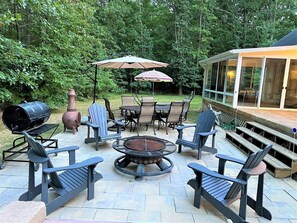 An outdoor patio with a fire pit, Adirondack chairs, a table with chairs, and a covered area with a large umbrella. - Riverwalk Retreat | Gather • Relax • Explore (Saugatuck)