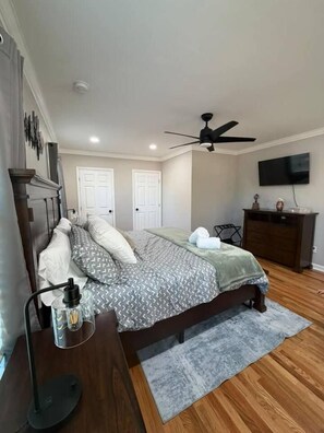 Un dormitorio con cama, escritorio, silla, cómoda, televisor y ventilador de techo.
