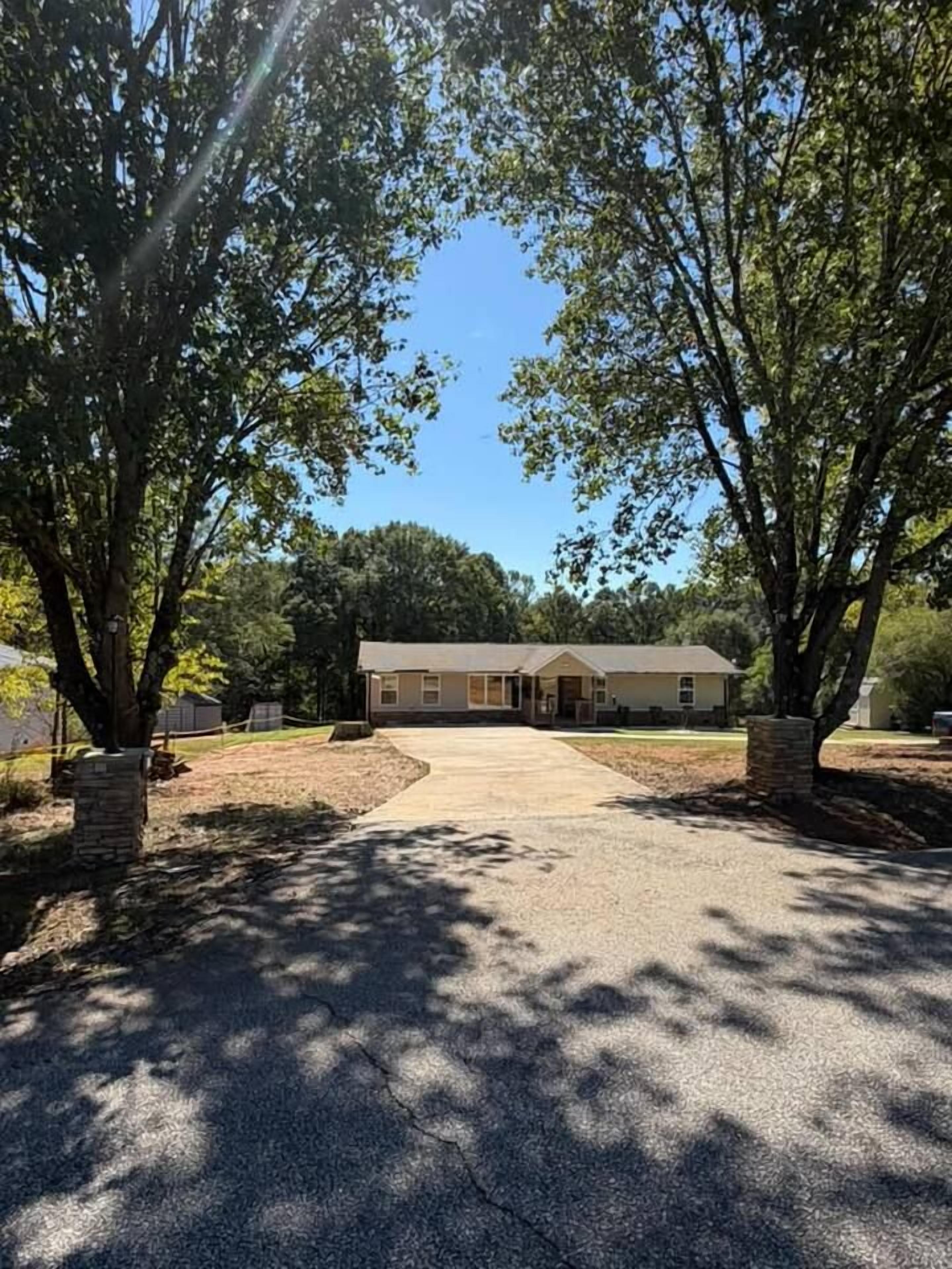 Une maison avec une allée menant à un garage, entourée d’arbres.