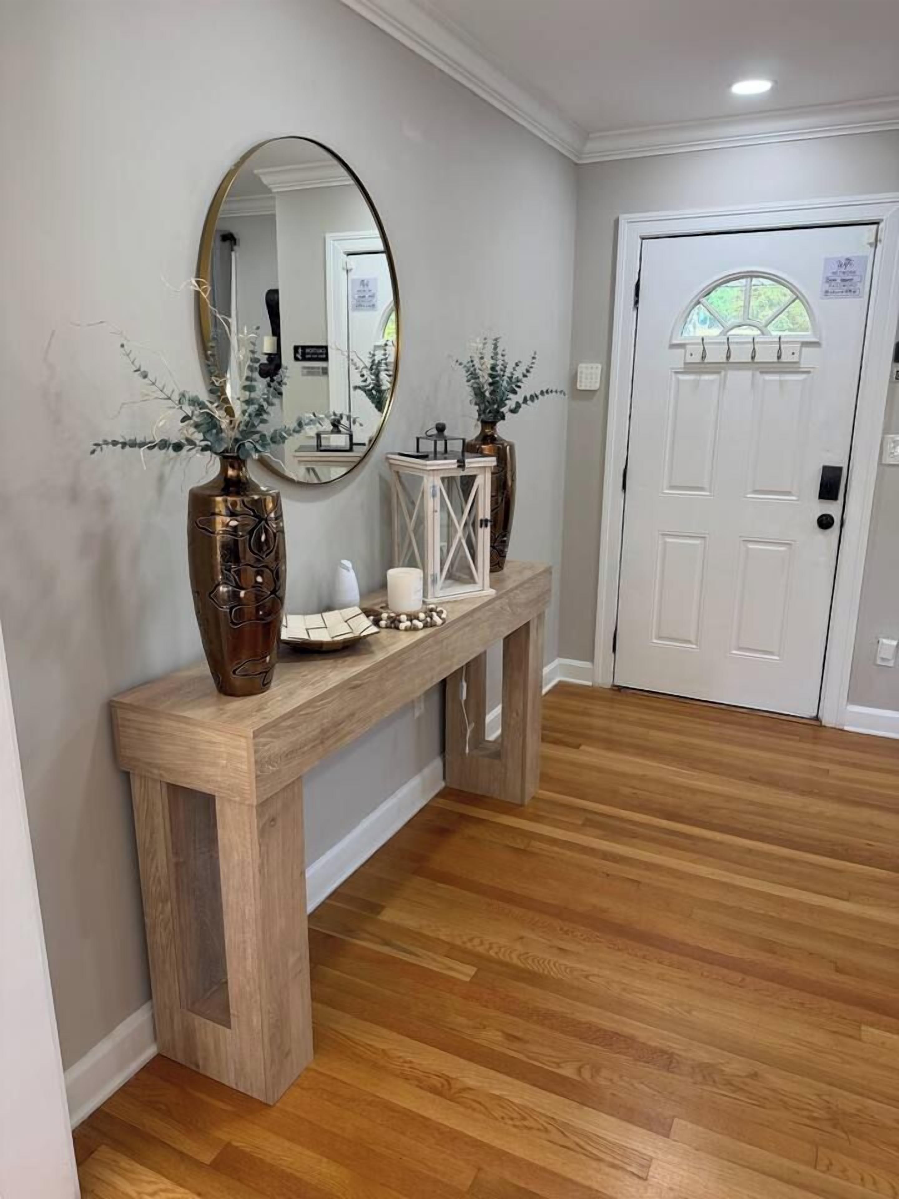 A hallway with a wooden console table, a mirror, and two vases with plants.
