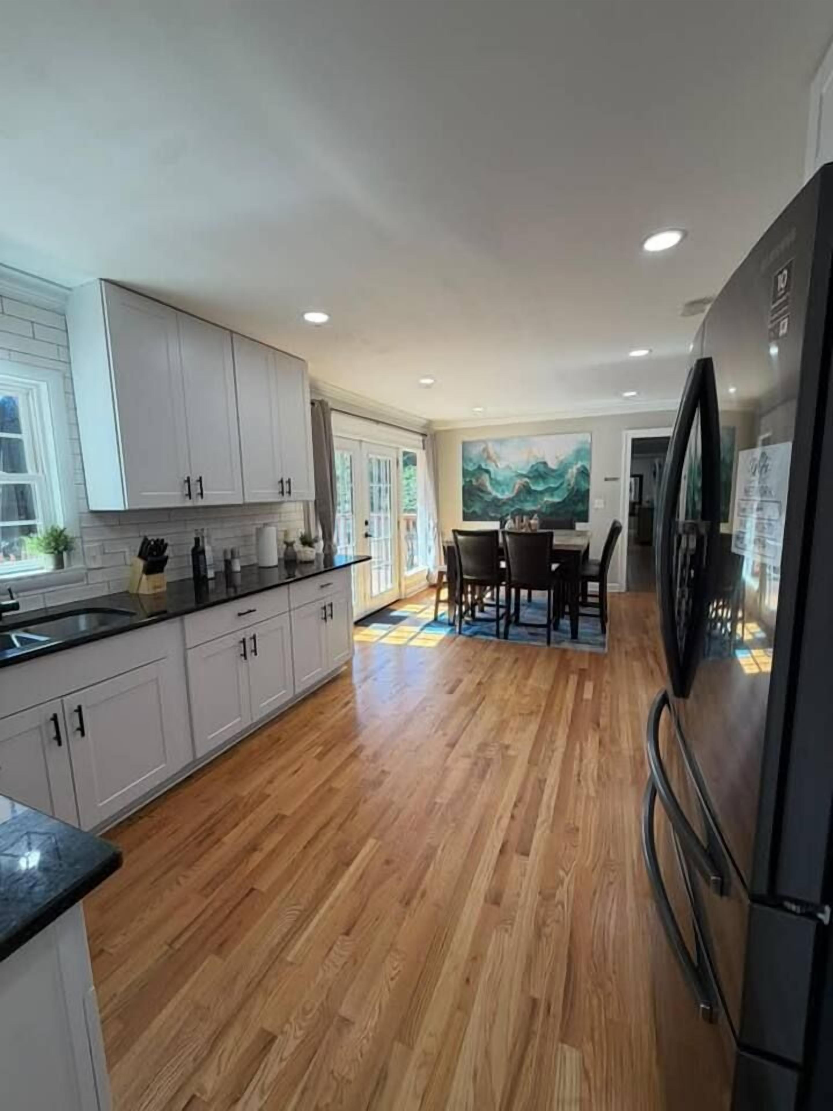A modern kitchen with wooden flooring, white cabinetry, and a dining area with a table and chairs.