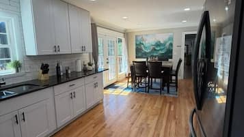 A modern kitchen with wooden flooring, white cabinetry, and a dining area with a table and chairs.