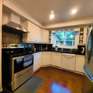 A kitchen with white cabinets, stainless steel appliances, and a window with a view of greenery. - Poolside Retreat | Private Pool, Hot Tub & Huge Deck in Niagara-on-the-Lake (Niagara-on-the-Lake)