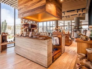 Un interior moderno con un mostrador de recepción de madera en el centro, estanterías con diversos objetos y vistas amplias a través de grandes ventanales.