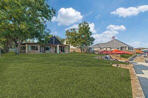 Área residencial com uma casa, um gramado frontal espaçoso, um espaço de estar coberto e um mastro com a bandeira americana.
