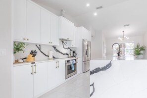 A modern kitchen with white cabinetry, a marble backsplash, and stainless steel appliances.