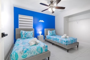 A hotel room with two beds, a ceiling fan, and a blue accent wall.