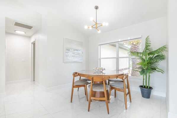 A dining area with a round table and chairs, a ceiling light fixture, a large window, and a potted plant.