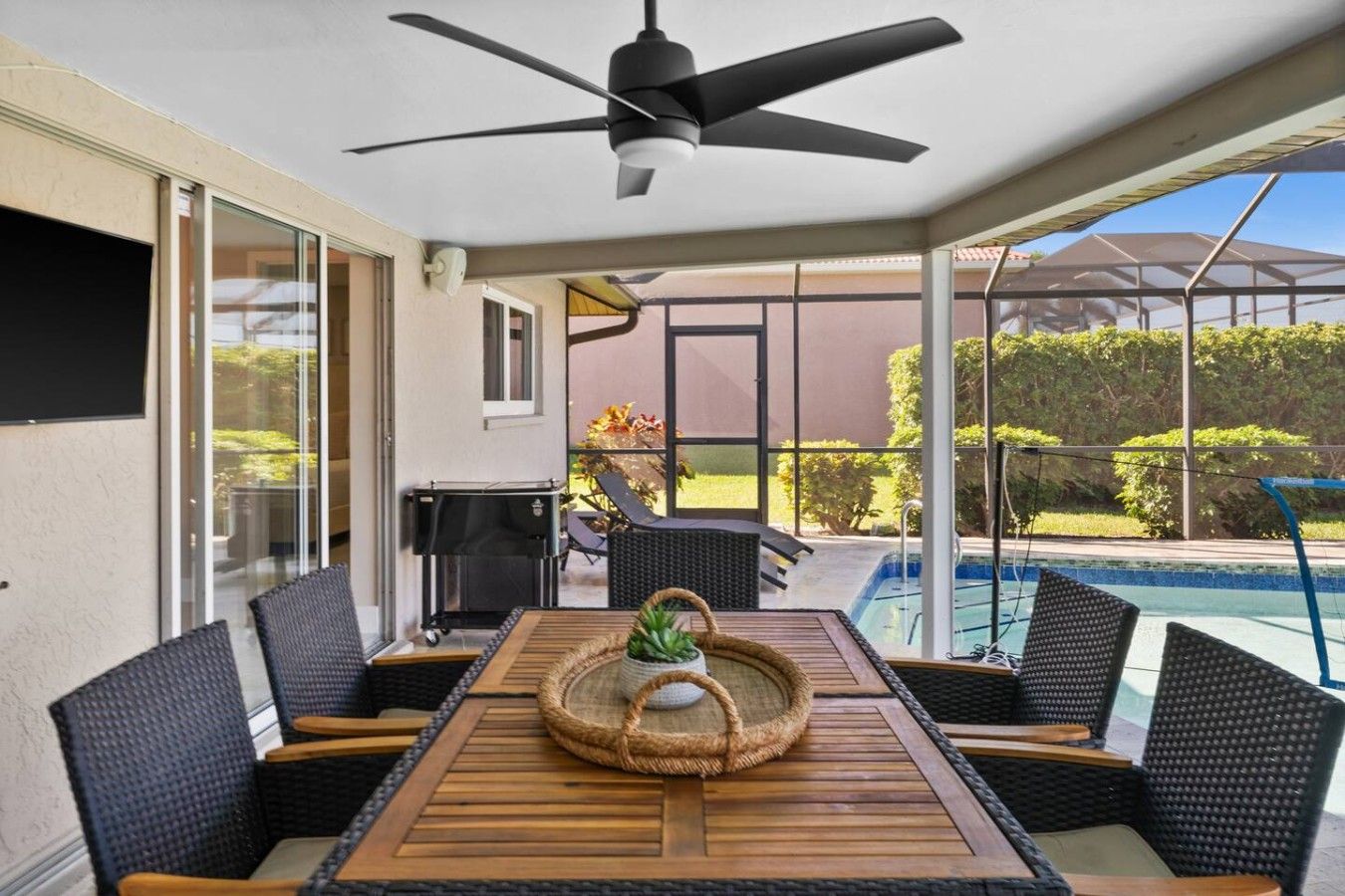 Eine Terrasse im Freien mit Tisch und Stühlen, einem Deckenventilator und Blick auf Pool und Garten.