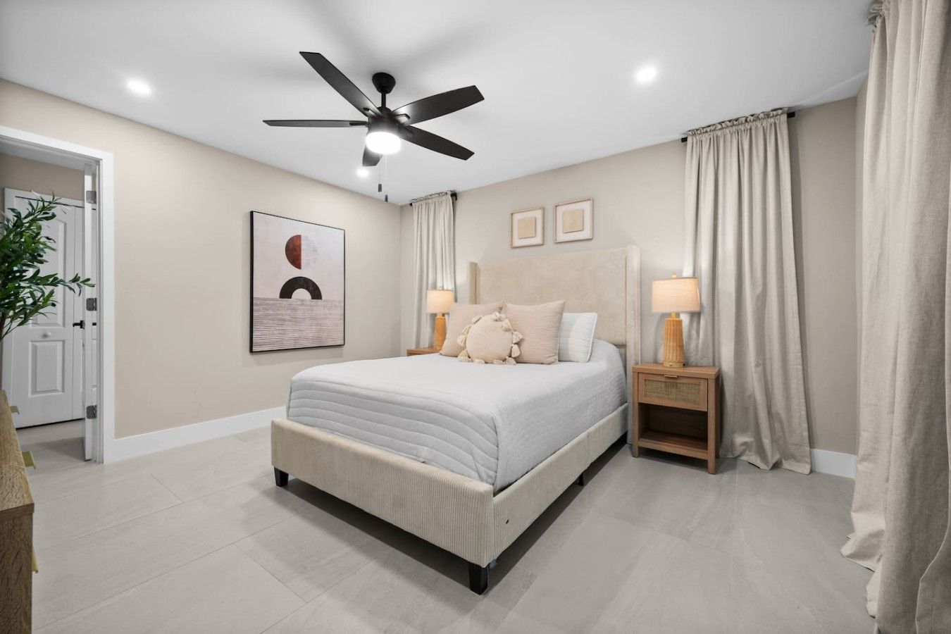 A bedroom with a bed, a ceiling fan, a nightstand with a lamp, and a door.