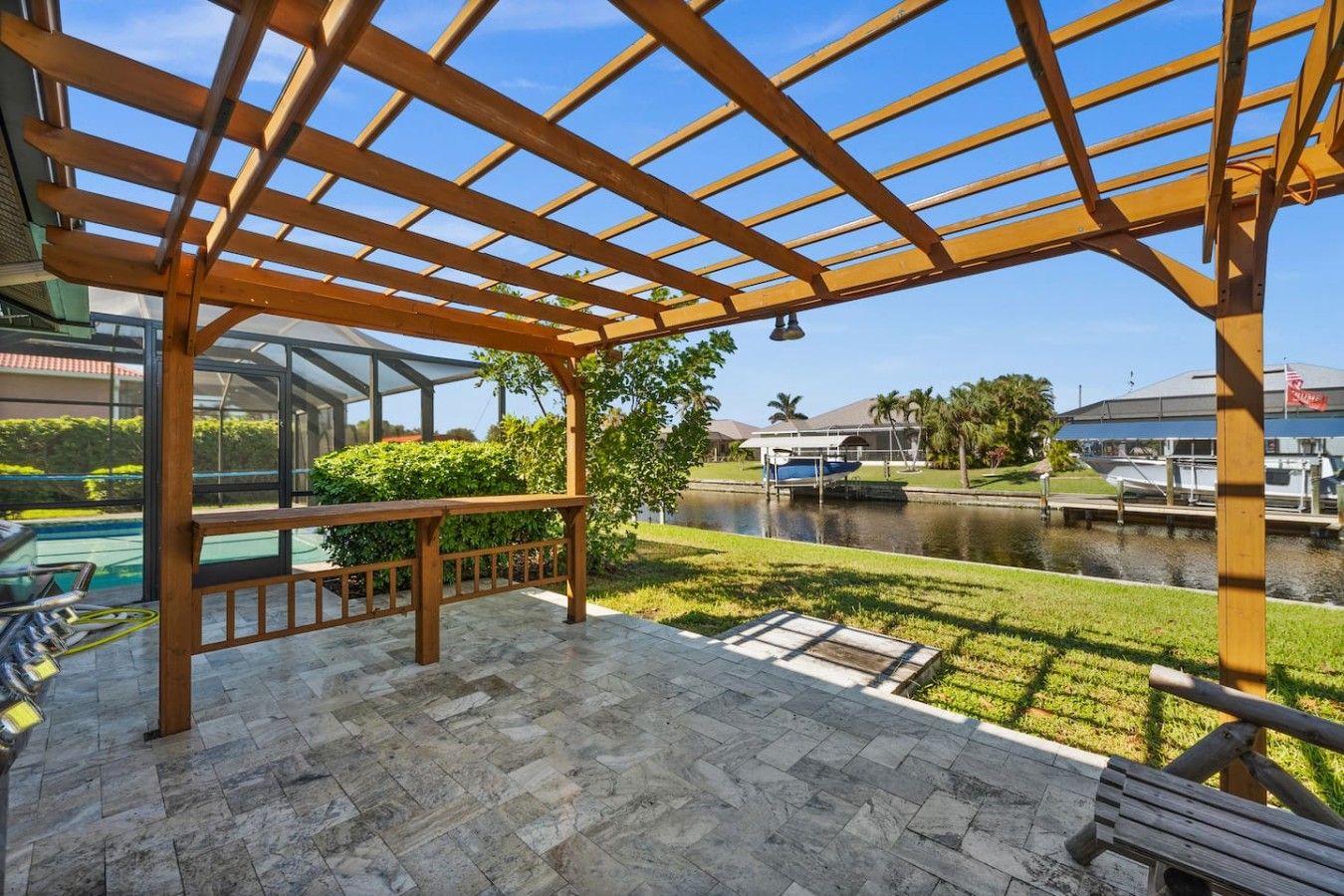 A covered outdoor area with a wooden pergola, a pool, and a view of a canal with boats.