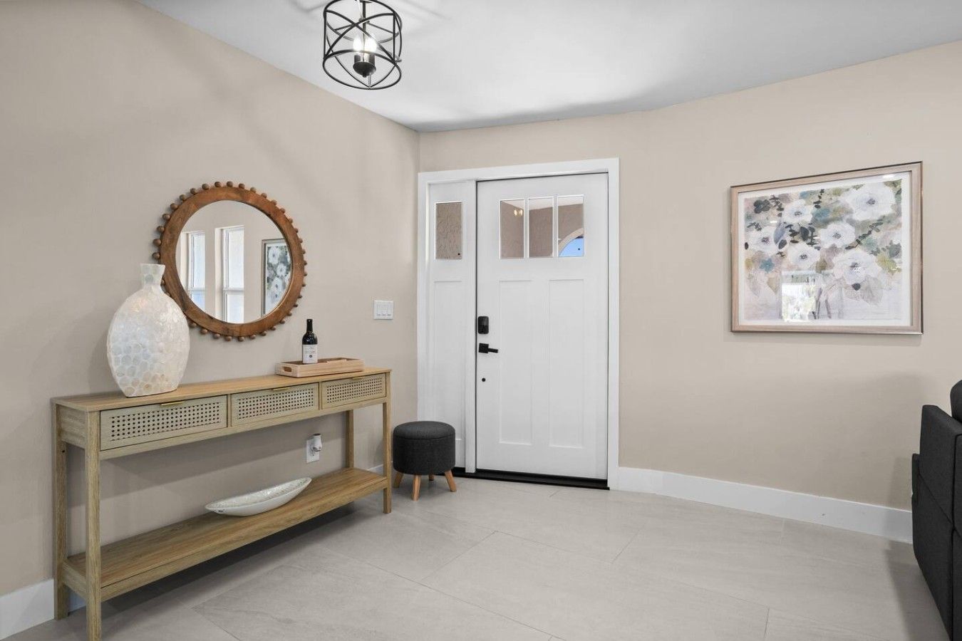 A hallway with a wooden console table, a round mirror, a white door, and a framed abstract painting.