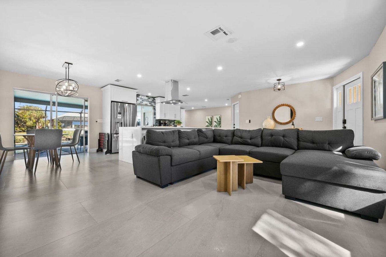 A modern living room with a sectional sofa, a dining area with chairs, and a kitchen in the background.