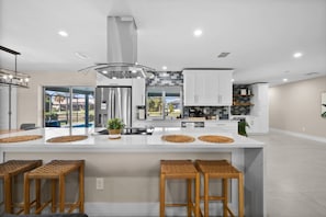 A modern kitchen with a central island, stainless steel appliances, and a view to the outdoors. - Modern Waterfront • Heated Pool • Private Dock (Cape Coral)