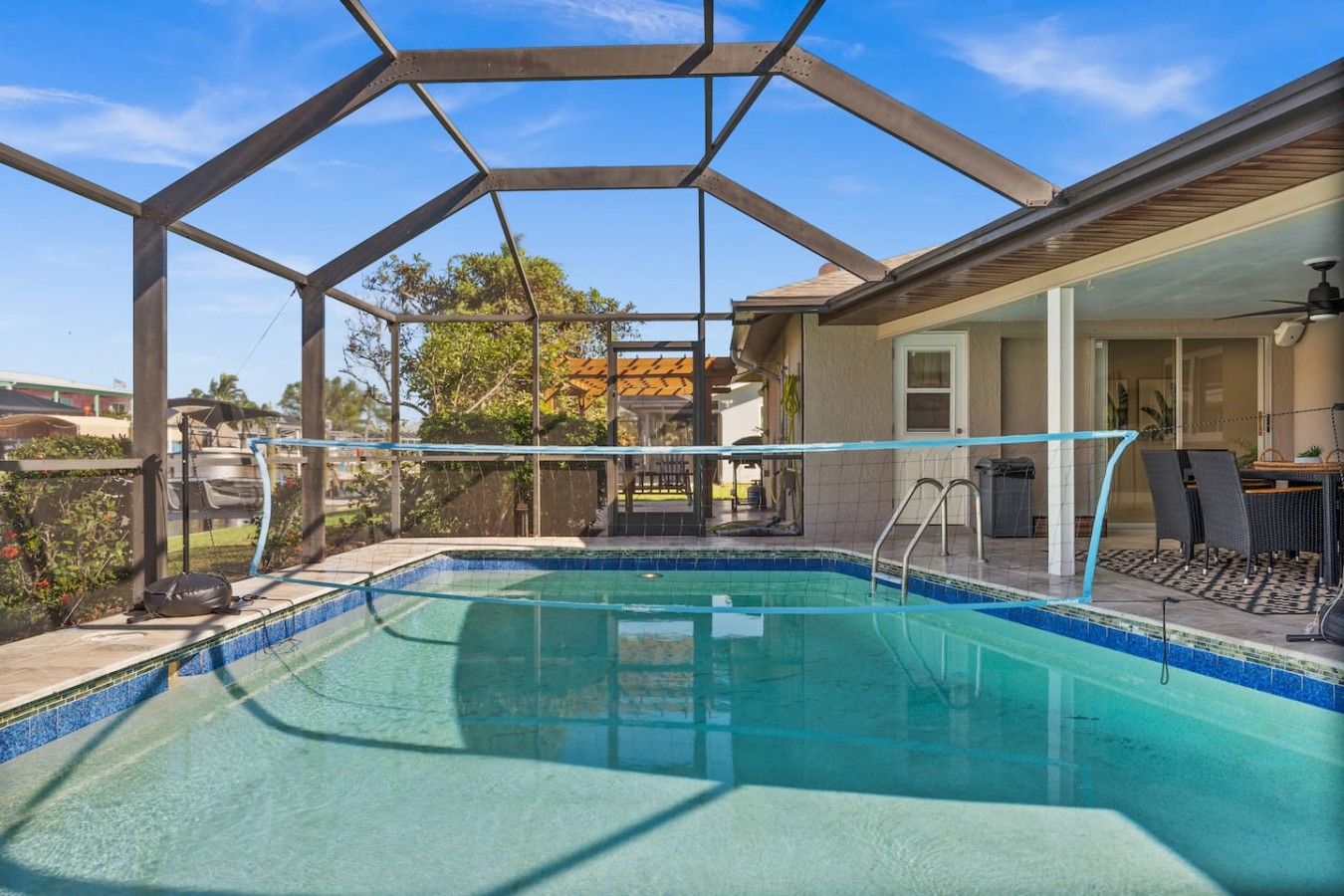 A swimming pool with a covered area, surrounded by a fence, and a patio with outdoor furniture.