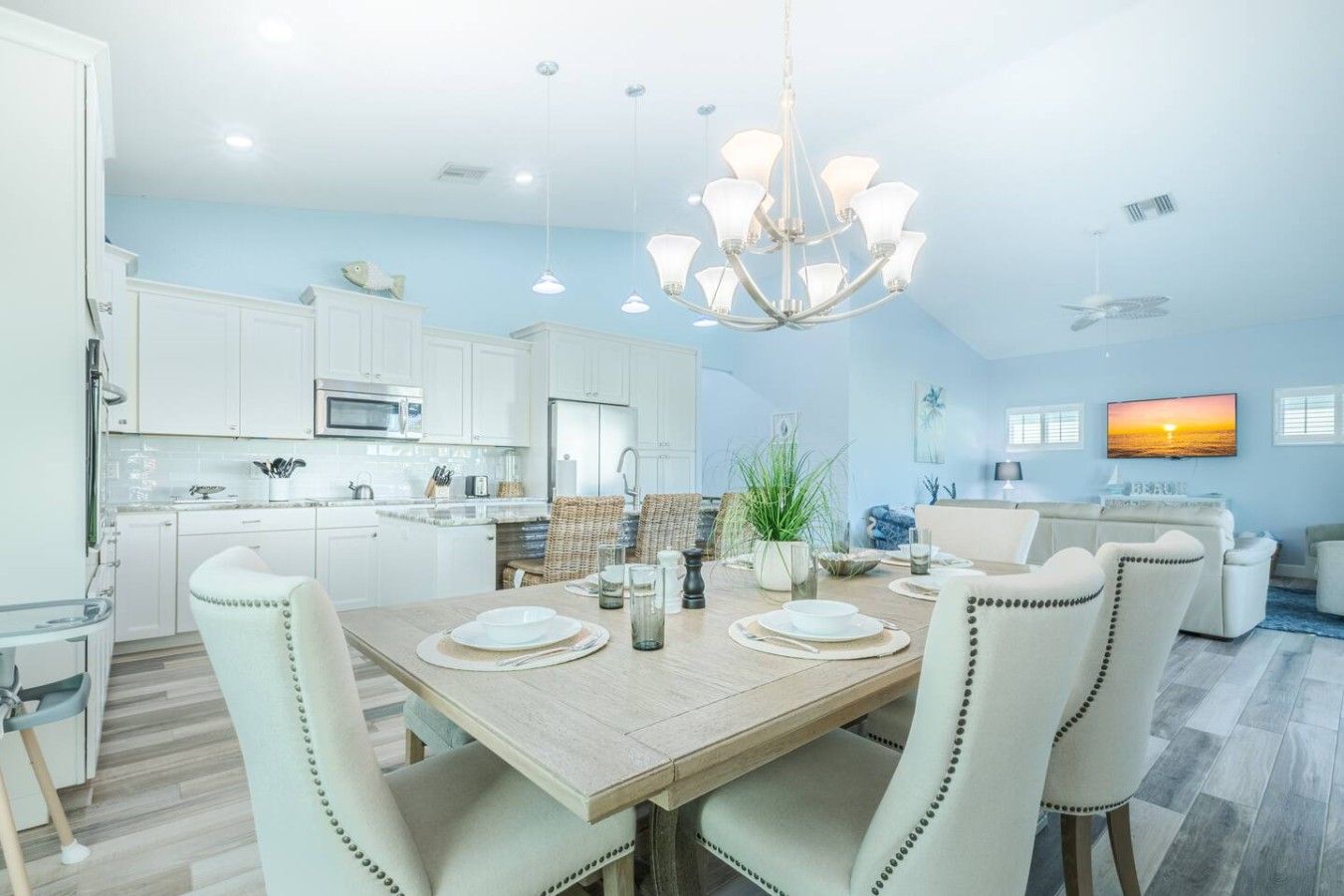 A modern kitchen with white cabinets, a dining area with a wooden table, and a living room with a TV.