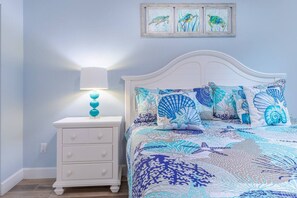 A bedroom with a white bed, a nightstand with a lamp, and a wall with three framed pictures. - RGB Pool & Game Room | Steps to Beach | 3BR Oasis (Fort Myers Beach)