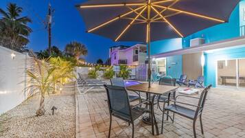 An outdoor patio with a table and chairs, a large umbrella, and a pool.