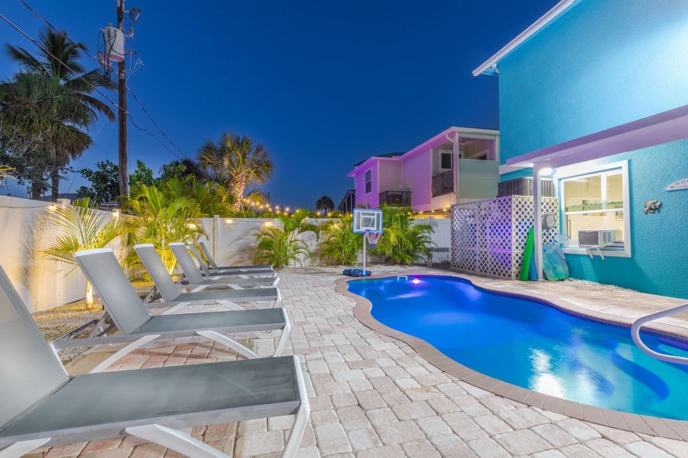 A swimming pool area with lounge chairs and a basketball hoop.