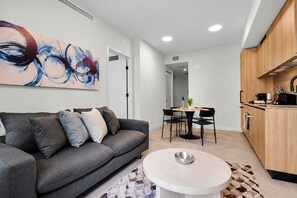 Ein modernes Wohnzimmer mit grauem Sofa, einem Esstisch mit Stühlen und einer Küchenzeile mit Holzschränken.