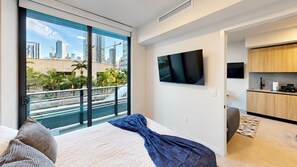 A modern hotel room with a large bed, a TV, a balcony with a city view, and a kitchenette. - NEW | High-Rise 1BR Den, Rooftop Pool & Gym 402 (Miami)