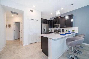 A modern kitchen with dark cabinets, a white island, and bar stools. - NEW | 2Bd Retreat with Game Room & Lazy River 9333 (Davenport)
