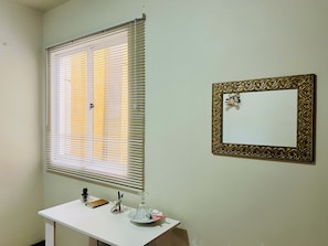 A room with a white desk, a framed mirror, and a window with blinds. - Pink Room near PUC Arena da Baixada, botanical garden and downtown Curitiba. (Curitiba)