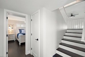 Eine Treppe mit Deckenventilator, ein Schlafzimmer mit Bett und Nachttisch sowie eine Tür zu einem weiteren Raum.