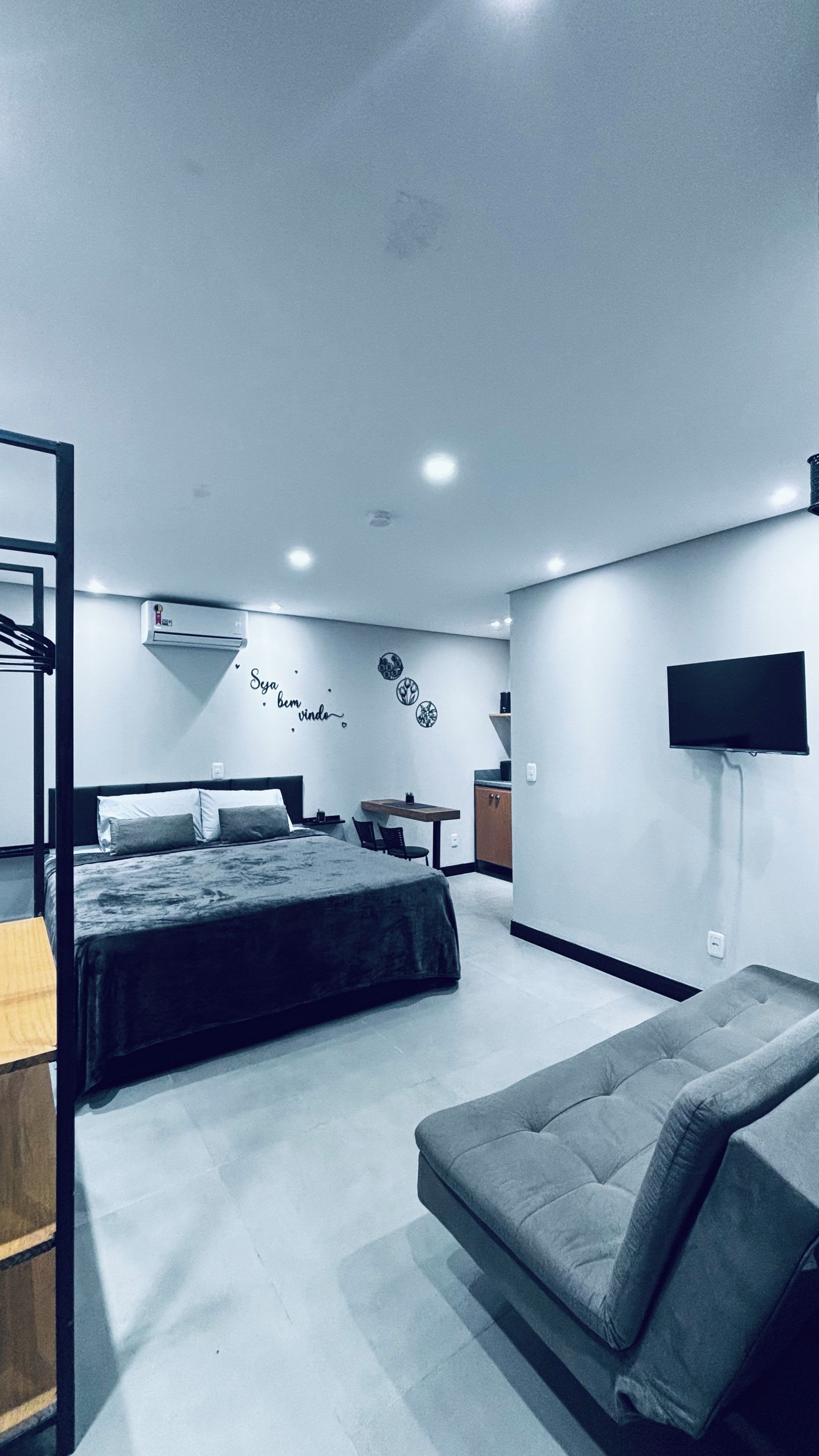Une chambre moderne comprenant un lit, un canapé, une télévision et un petit coin cuisine.