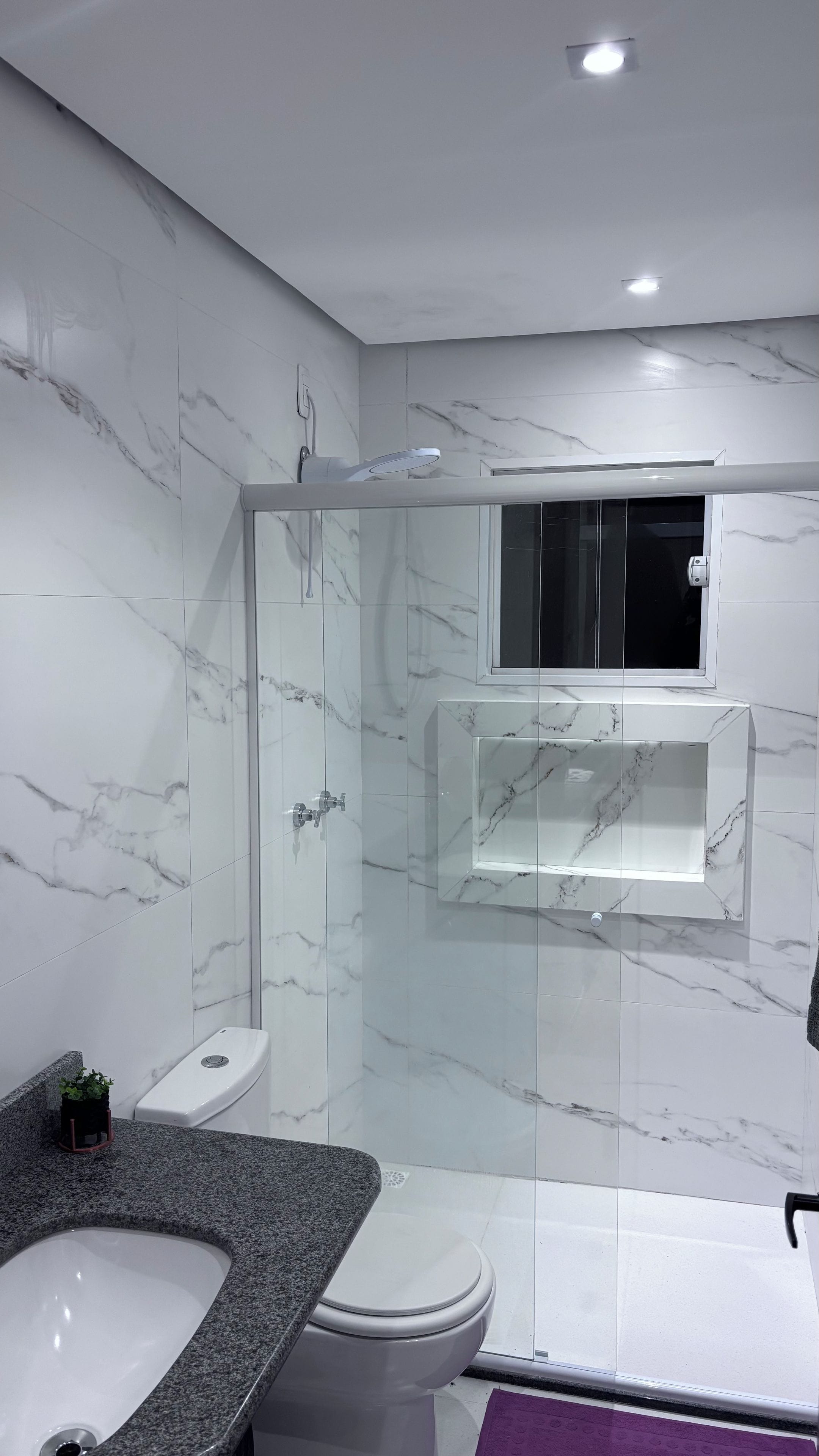Une salle de bain moderne avec une douche à parois de verre, des toilettes blanches et un lavabo surmonté d’un plan de travail en granit.