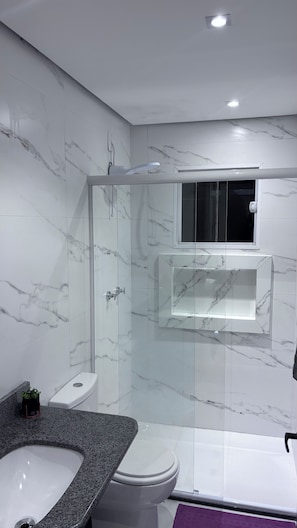 Un bagno moderno con doccia vetrata, vaso bianco e lavabo su piano in granito.