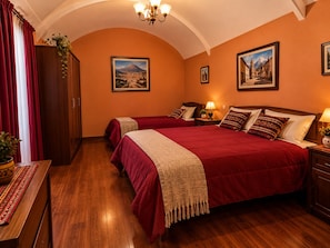 Habitación de hotel con una cama grande, dos mesitas de noche, suelo de madera y un candelabro.