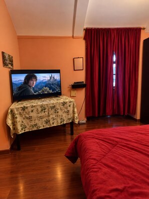 A room with a television on a table, a bed, and a window with red curtains. - Casa Naranja céntrico  (Villa Imperial de Potosí)