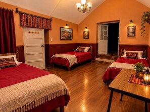 A room with three beds, a wooden table, a chandelier, and a door leading to another room. - Casa Naranja céntrico  (Villa Imperial de Potosí)