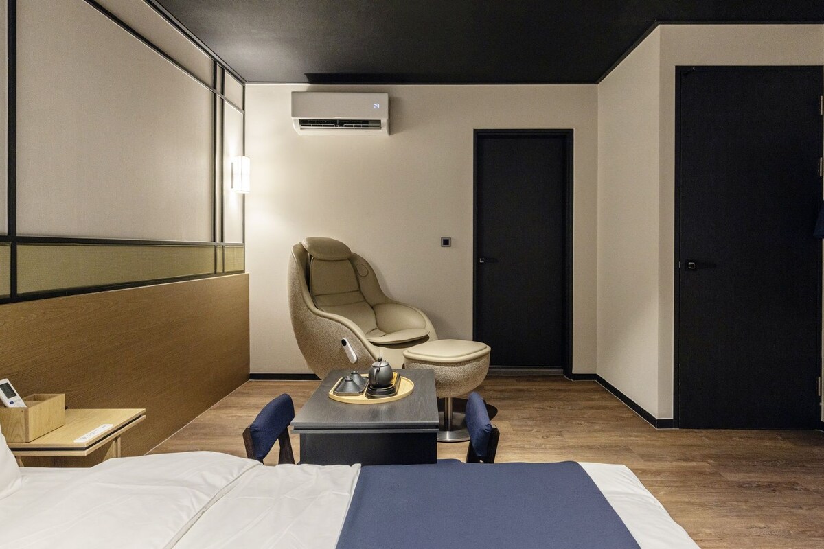 Une chambre d’hôtel avec un lit, une chaise, une petite table avec un service à thé, une armoire et une porte.