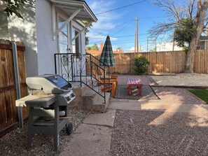 Ein Garten mit Grill, Holzterrasse, Gartenmöbeln und einem eingezäunten Bereich.