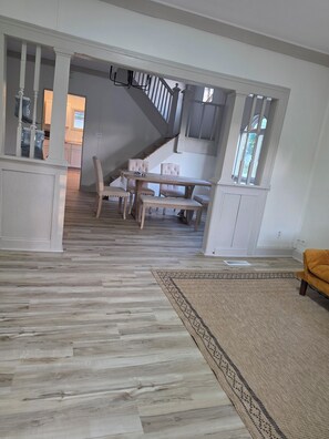 A spacious living area with a wooden floor, a dining table with chairs, and a staircase leading to another level. - Cozy 2-Bedroom Home | Near Riverside Park (Indianapolis)