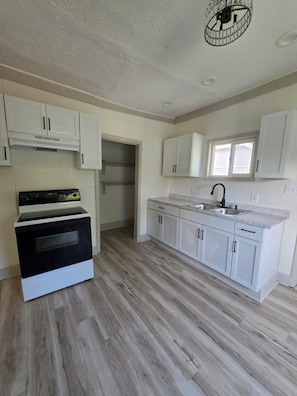 A kitchen with white cabinets, a black oven, and a window above the sink. - Cozy 2-Bedroom Home | Near Riverside Park (Indianapolis)